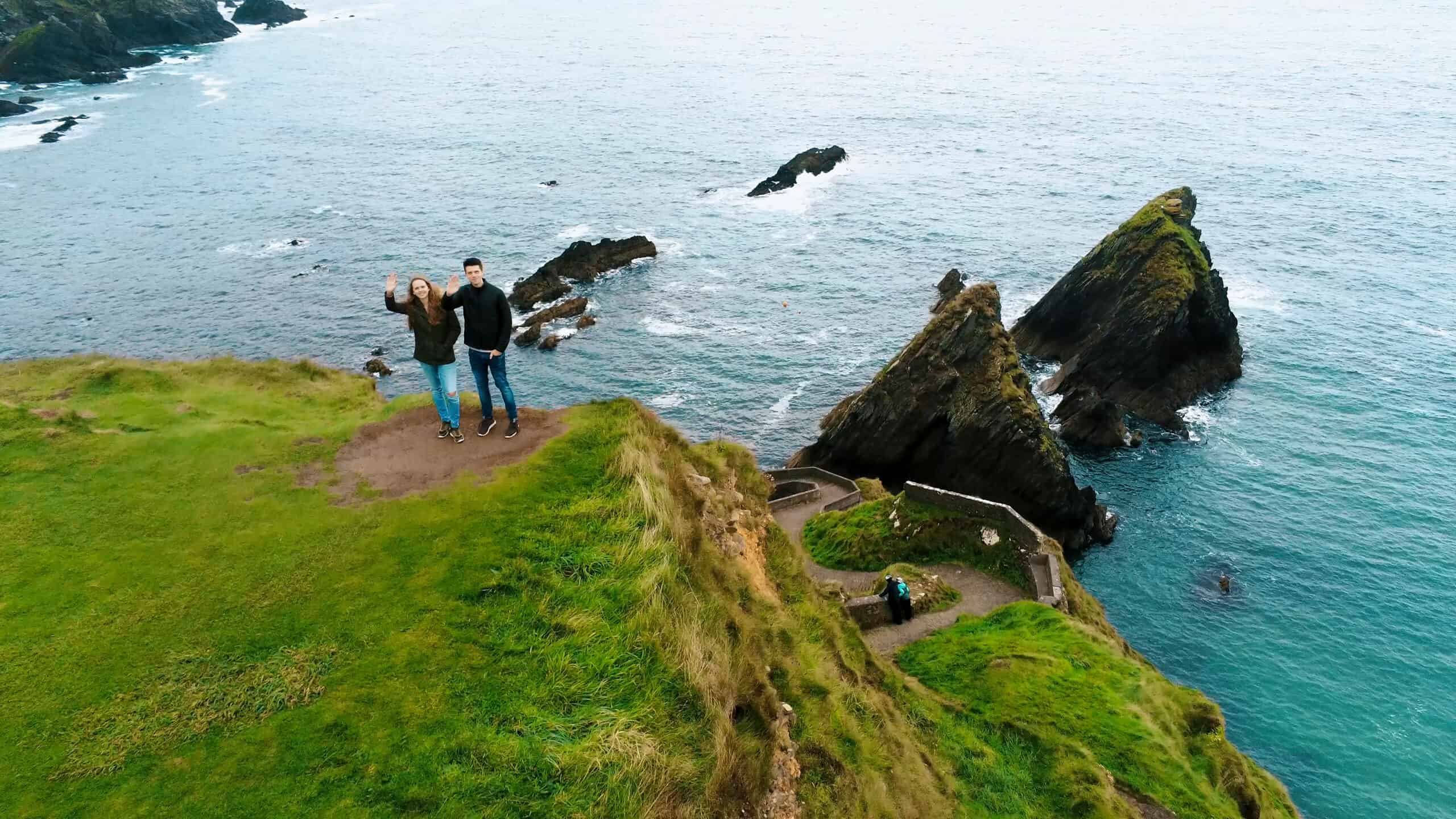 Ein Paar winkt an der Küste Irlands mit Blick auf das Meer.