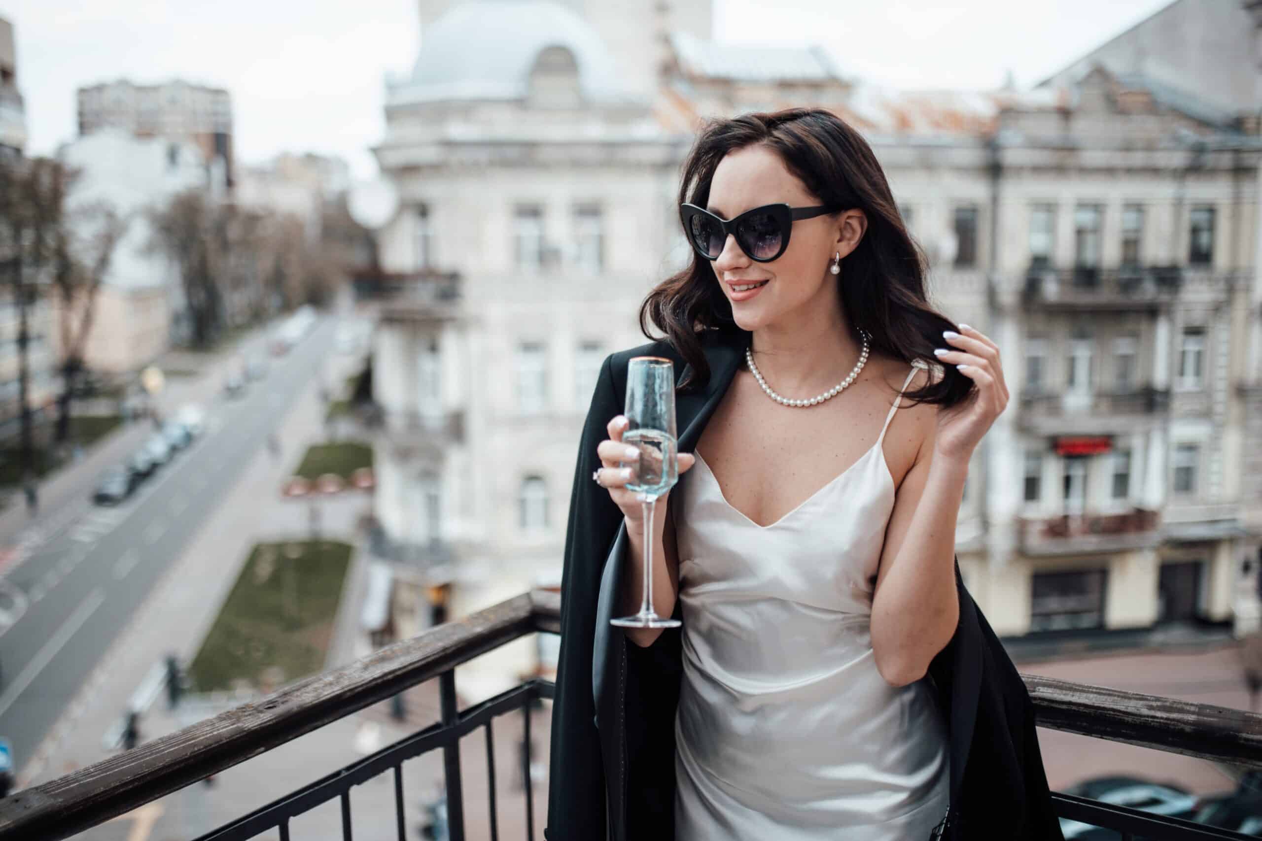 Frau mit Champagner auf Balkon vor Stadtkulisse